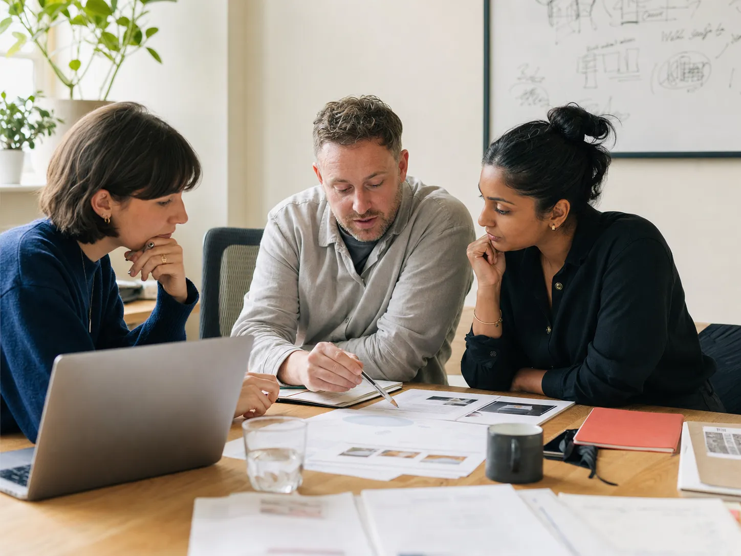 A small team reviewing printed reports and sketches together around a table.